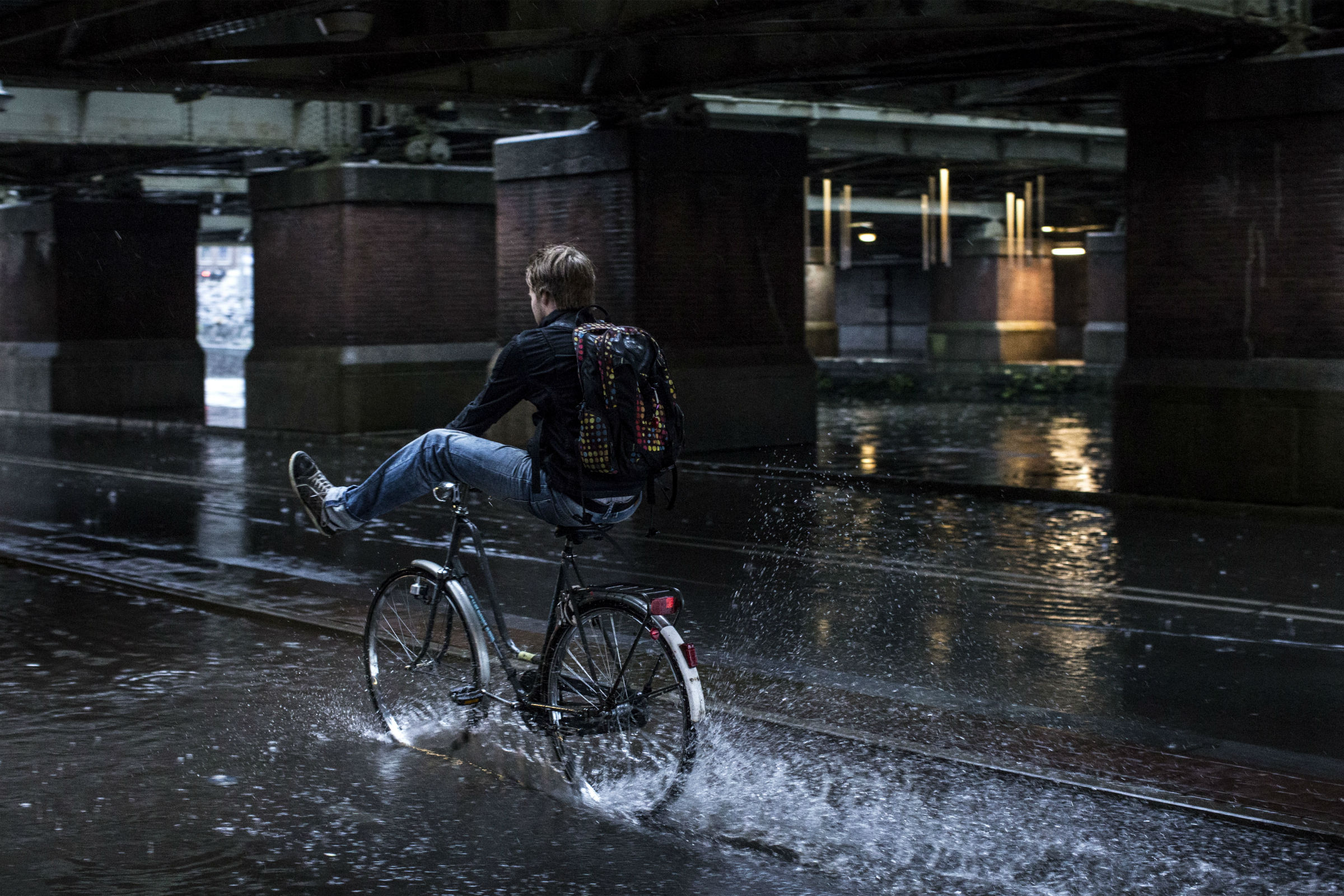 Man fietst door de regen met z'n benen op zijn stuur