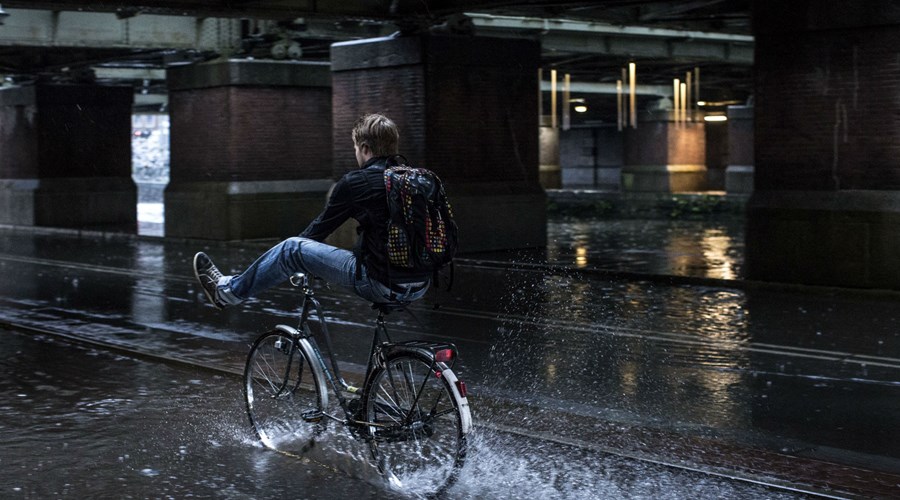 Man fietst door de regen met z'n benen op zijn stuur